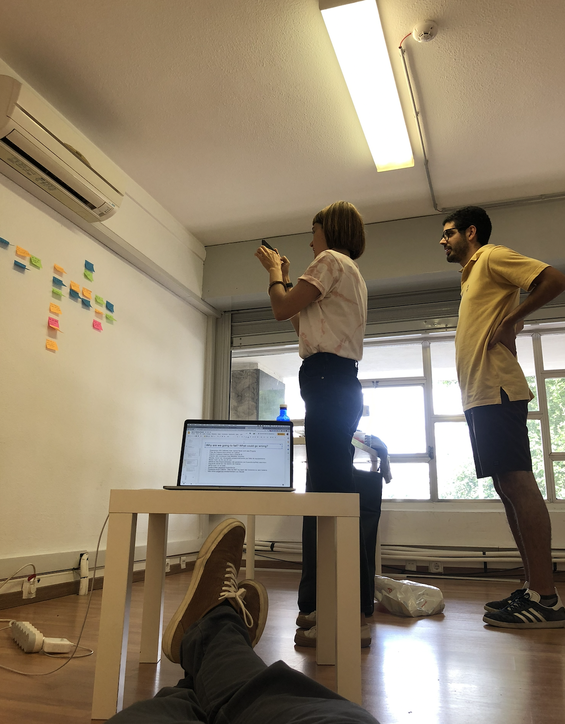 Creative workspace with woman on desk taking photo, sticky-note wall collaboration